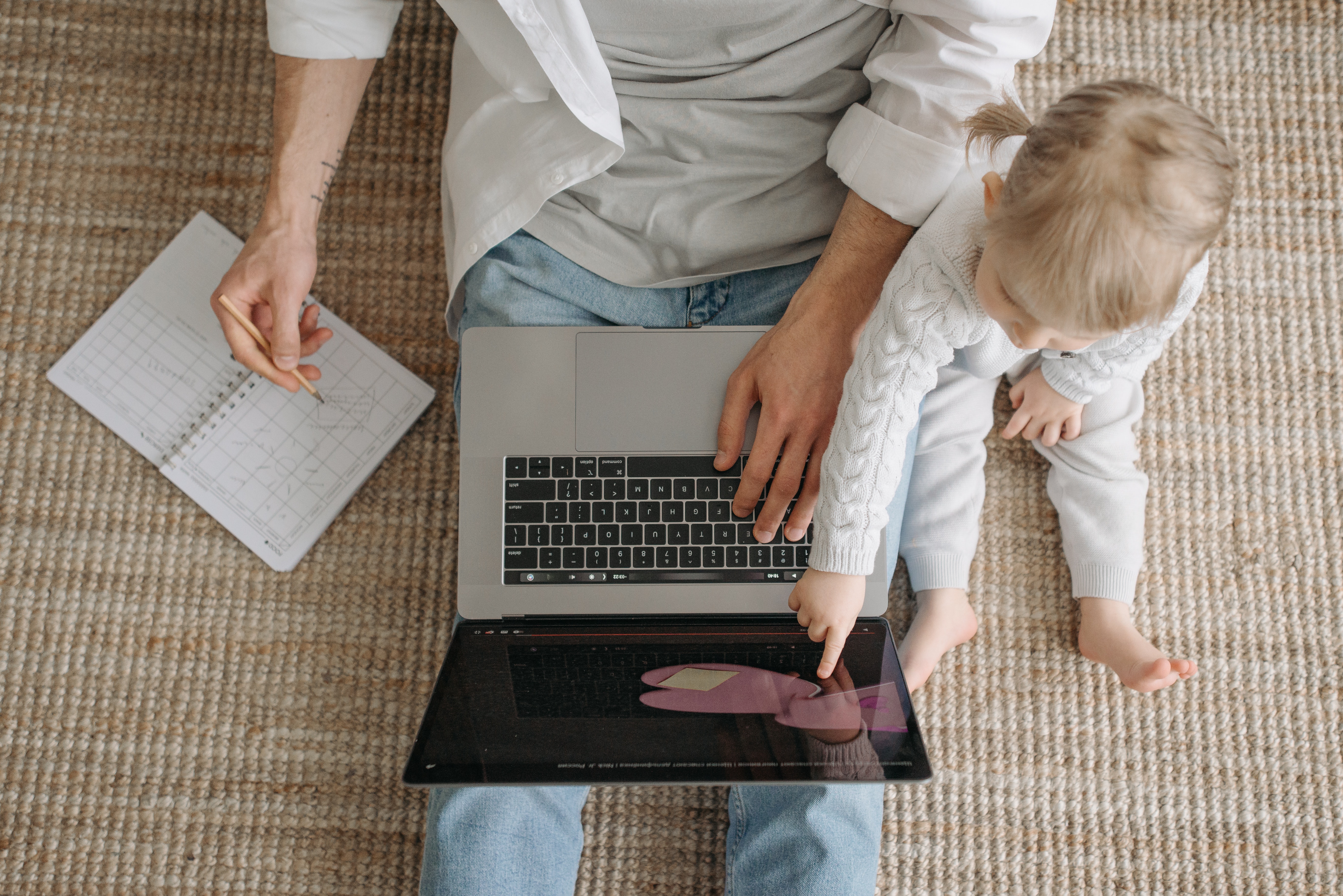 Stock photo featuring parent and child on floor with laptop and notebook open.