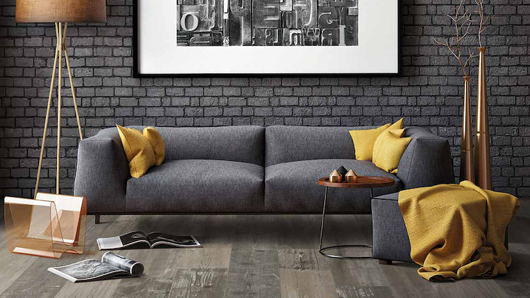 rustic wide planked wood look luxury vinyl plank floors in a modern living room with grey brick walls and grey couch